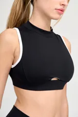 Top deportivo negro con escote alto, abertura en el centro del pecho y ribete blanco en sisas y cuello.