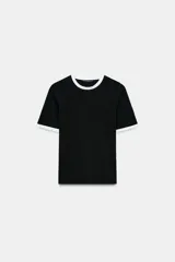 Camiseta negra de manga corta y cuello redondo, con ribetes de tricot blanco con perlas aplicadas en el cuello y los puños de las mangas.