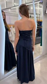 Vestido largo azul marino strapless con escote recto, corte ajustado en el torso y falda larga con tajo lateral profundo y detalle de volados en la parte inferior.