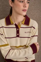 Buzo de punto con cuello polo y cierre frontal de tres botones. Diseño a rayas horizontales en tonos crema, bordó y mostaza, con detalle de bordado en el pecho.