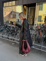 Cartera tipo hobo de cuero color borgoña con asa superior anudada.