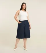 Bermuda tipo jorts de corte amplio y tiro medio, confeccionada en denim de algodón azul oscuro. Presenta diseño de cinco bolsillos, cierre frontal con botón y costuras en tono contrastante.