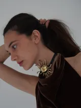 Collar tipo gargantilla con tiento de cuero negro y un dije grande en forma de sol de bronce con relieve en el centro.