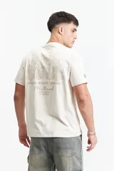 Remera de manga corta color beige claro con cuello redondo y fit regular. Estampado grande en la espalda con diseño de abanico de plumas de pavo real en tonos beige/dorado, y texto debajo que dice "STARS MUSIC SOUND", "Mistral" y "LOS ANGELES CALIFORNIA".