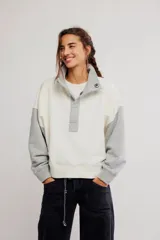 Buzo de frisa con diseño colorblock en tonos blanco y gris, cuello alto con botones a presión frontales, mangas largas raglán y puños y cintura acanalados.