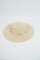 Sombrero de paja tejido color beige, de ala ancha y copa redonda, decorado con una sarta de caracoles marinos colgantes.