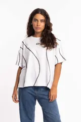 Remera blanca de corte boxy fit con costuras negras a la vista que recorren la prenda de forma ondulada. Tiene cuello redondo y mangas cortas.