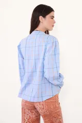 Camisa de manga larga con estampado de cuadros en tonos celestes, naranjas y verdes. Presenta un diseño con pliegues verticales en el frente, cuello redondo y cierre frontal con botones. Las mangas tienen un ligero frunce en los hombros y puños abotonados.