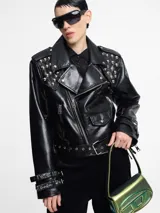 Chaqueta biker negra de cuero sintético con tachas plateadas en los hombros y solapas, cierre asimétrico con cremallera, cinturón ajustable con hebilla y detalles metálicos.