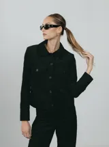 Chaqueta corta negra de pana de algodón con cuello clásico, cierre frontal con botones, dos bolsillos de parche en el pecho y mangas largas.