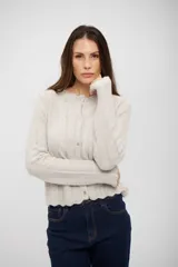 Saco de punto gris claro con textura acanalada, cuello redondo, cierre frontal con botones y bordes con terminación ondulada.