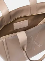 Cartera tote Calvin Klein color beige con asas dobles de mano y cierre de cremallera superior. Presenta el monograma de la marca grabado en el frente.
