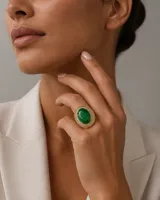 Anillo de plata esterlina con baño de oro, presenta una esmeralda reconstruida de corte ovalado en el centro, rodeada por un halo de circones en corte baguette.