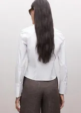 Camisa blanca de cuello camisero clásico y mangas largas, con cierre frontal de botonadura oculta.
