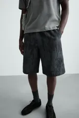 Bermuda de corte relajado, color gris oscuro con efecto tie-dye o textura irregular. Presenta cintura elástica ajustable con cordón y bolsillos laterales y traseros de plastrón.