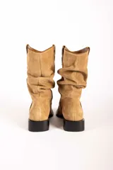 Bota de caña media confeccionada en gamuza color tostado, con diseño arrugado en la caña, punta fina y suela plana con pequeño taco cuadrado.