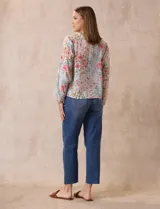 Blusa de gasa plisada con estampado floral en tonos rosas y celestes. Presenta cuello a la base con escote en V y lazo de ajuste frontal, mangas largas con puños elásticos y corte recto.