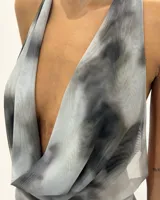 Vestido midi de tela semitransparente con estampado abstracto en tonos grises y negros. Presenta un escote halter profundo con drapeado frontal y diseño ajustado al cuerpo.