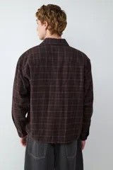 Camisa de corte boxy confeccionada en franela a cuadros, con cuello clásico, cierre frontal de botones, bolsillo en el pecho y puños abotonados.