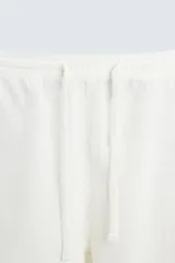 Bermuda de algodón color blanco, de corte relajado (relaxed fit), con cintura elástica ajustable mediante cordón. Posee bolsillos laterales y un bolsillo trasero de plastrón. Presenta un bordado en contraste en la pernera.