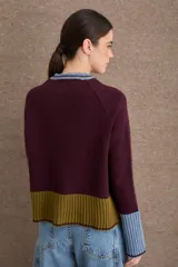 Cardigan de punto con diseño color block en tonos bordó, verde oliva y beige. Presenta cuello redondo con detalle en celeste, cierre frontal con botones y puños acampanados en color beige.