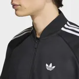Campera deportiva Adidas modelo SST Adicolor Classics Cotton Twill, color negro con las clásicas tres tiras blancas en las mangas y el logo del Trifolio bordado en el pecho. Cuenta con cierre frontal y bolsillos.