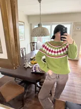 Sweater tejido a mano en mohair, de color marrón con diseño de canesú estampado con corazones fucsias y detalles geométricos en tonos beige y rosado. Presenta cuello redondo y mangas largas.