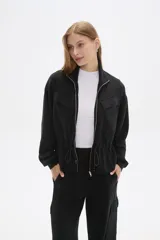 Campera negra de manga larga con cierre frontal, bolsillos frontales con solapa y cordón ajustable en la cintura.