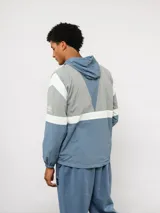 Campera de nylon Umbro con capucha, cierre frontal y diseño de bloques de color en gris, blanco y azul. Puños y dobladillo elásticos.