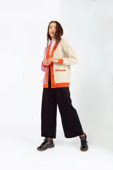 Cárdigan tejido de punto grueso, con diseño color block en gris, blanco y beige. Tiene cuello en V, cierre frontal con botones y un bolsillo de parche.