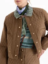 Chaqueta matelaseada color marrón, de corte recto y largo a la cadera, con cuello redondo, cierre frontal con broches dorados y bolsillos plaqué en el delantero.