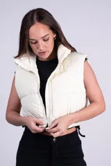 Chaleco puffer corto color blanco, con cuello elevado y cierre frontal. Cuenta con diseño acolchado y bolsillos laterales.