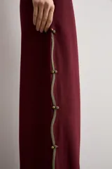 Pantalón ancho color bordó de talle alto, con abertura lateral decorada con ribete contrastante y cierre de botones tipo nudo chino.