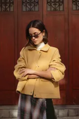 Chaqueta de lana afieltrada color amarillo, con cuello camisero, cierre frontal con broches a presión y bolsillos delanteros. Presenta un diseño de corte holgado con una apertura en la espalda que aporta movimiento.