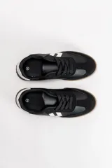 Zapatilla acordonada de estilo urbano, confeccionada en una combinación de materiales sintéticos en color negro, con detalles en blanco en los laterales y en el talón, y suela de goma color caramelo.