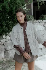 Saco de punto color crudo con diseño de flecos en el frente y mangas, cierre frontal con botones y cuello redondo.