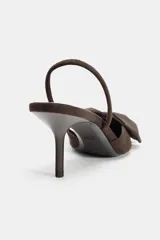Zapato destalonado de tacón medio con punta fina, acabado en color marrón y detalle de lazo decorativo en la parte delantera. Cuenta con una tira elástica trasera para mayor sujeción.