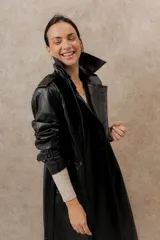 Trench largo de ecocuero negro, con cuello clásico, cierre cruzado con botones laterales y cinturón ajustable.