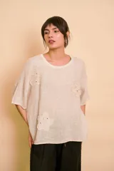 Blusa holgada color beige con mangas cortas y cuello redondo. Presenta apliques bordados con detalles de perlas y lentejuelas en el frente.