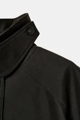 Trench oversize color negro de la colección Zara Woman, confeccionado en hilatura con mezcla de algodón. Presenta cuello solapa, manga larga ajustable con trabillas, bolsillos delanteros y cierre frontal con botones.