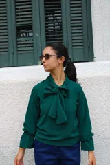 Blusa verde de manga larga con cuello tipo lazo, confeccionada en tela con textura ligera y corte recto.