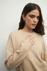 Sweater de tejido de punto color marrón, con cuello redondo y detalles de calados decorativos en el cuello y las mangas. Presenta un diseño de corte recto y manga larga.