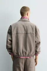 Cazadora de algodón de corte relajado, color marrón grisáceo con efecto lavado. Presenta cuello solapa con tachas metálicas, cierre frontal de cremallera, bolsillos de plastrón en la cadera y puños y bajo elásticos.