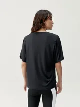 Camiseta holgada de manga corta, color blanco roto, con cuello redondo y un estampado sutil de letras en tono gris claro.