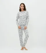 Pijama de dos piezas confeccionado en tejido de punto, compuesto por una blusa de manga larga con cuello redondo y puños ajustados, y un pantalón recto con cintura elástica. Presenta un estampado continuo de moñitas sobre fondo gris.