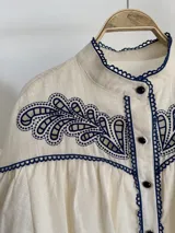 Blusa de algodón off white con cuello mao, botones frontales y mangas globo. Cuenta con canesú destacado con bordado floral en color azul marino.