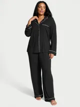 Pijama largo de modal negro, compuesto por una camisa de manga larga con botones frontales y ribetes blancos, y pantalón recto con cintura elástica y cordón ajustable.