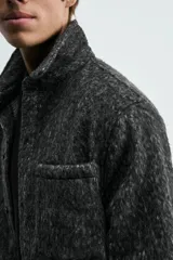 Sobrecamisa de corte relajado confeccionada en tejido con textura efecto pelo. Presenta diseño de cuadros en tonos verde y negro, cuello solapa, cierre frontal con botones, manga larga con puños abotonados y un bolsillo de plastrón en el pecho.