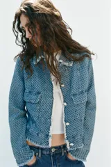 Chaqueta de denim de corte clásico con textura perforada, cuello solapa, bolsillos delanteros de plastrón, cierre frontal con botones a contraste y detalles de flecos en los bordes.
