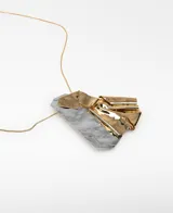Collar largo con cadena metálica dorada y un dije geométrico asimétrico compuesto por piezas metálicas combinadas en tonos plateado y dorado con efecto de pliegues.